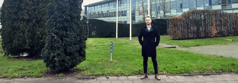 Trevor Terry stands on a patch of grass. In the background is a building with large glass windows